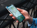 An outdoor close-up of a hand holding a smartphone displaying a map application.