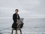 A person with a laptop sitting on a ladder by the ocean, symbolizing remote work.
