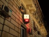 Illuminated wall clock showing time and temperature on a building facade at night.