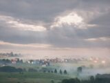A serene misty morning in Kupres, Bosnia with sunrays piercing through clouds over the village.