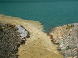 A captivating view of muddy water merging with clear blue river water at a rocky riverbank.