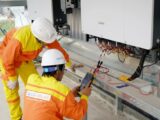 Two electrical engineers installing and testing solar power systems wearing safety gear at a construction site.