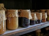 Assorted preserved foods in glass jars on a wooden shelf, showcasing traditional storage methods.