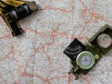 Overhead view of a map with a compass and flashlight showing navigation tools.