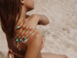 Close-up of a woman applying sunblock on her shoulder on a sunny beach day in summer.