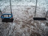 A pair of empty swings covered with snow in a winter playground, creating a serene and isolated atmosphere.