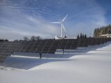 Solar panels and wind turbine in a snowy landscape, showcasing renewable energy sources.
